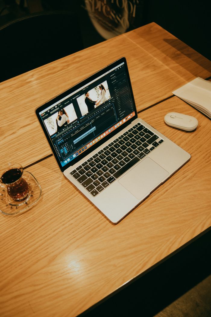 about-us-02 A laptop on a wooden table in a coffee shop, displaying video editing software for creative work.